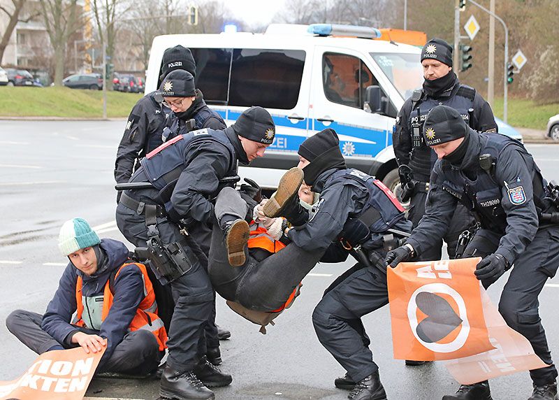 Nachdem die Aktivisten mehrfach aufgefordert wurden, die Fahrbahn zu räumen, wurden zunächst die nicht festgeklebten Personen von Polizeikräften weggetragen.