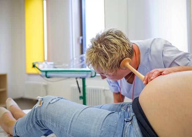 Hebamme Gabriele Fischer hört mit einem Pinard-Rohr die fetalen Herztöne ab.