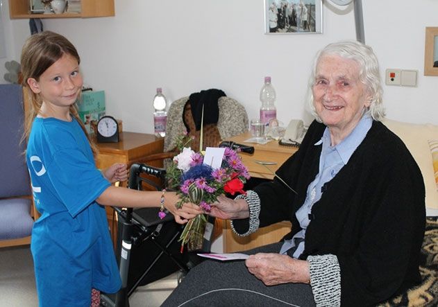 Lilly Scheller (8 Jahre) übergibt einen selbstgebundenen Blumenstrauß und Grußkarte an Frau Riesenberg, Bewohnerin des Altenzentrum Luisenhaus.