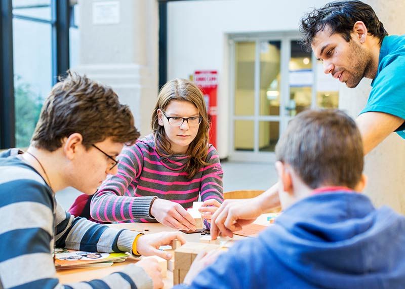 Ein Student hilft Schülerinnen und Schülern bei Mathe-Rätseln.