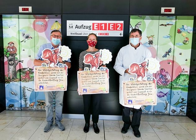 Der letzte Akt nach über vier Jahren Arbeit: Schilder weisen auf die fertige Gestaltung der Kinderklinik Jena hin. Auf dem Bild zu sehen (v.l.): Prof. Felix Zintl, Vorsitzender der Kinderhilfestiftung Jena, Künstlerin Wanda Gaertner und Prof. James Beck, Direktor der Klinik für Kinder- und Jugendmedizin.