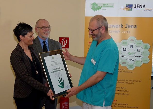 Bürgermeister Frank Schenker und Dr. Sabine Trommer, Teamleiterin Hygiene der Stadt Jena und Koordinatorin des MRE-Netzwerks Jena, überreichen Dr. Ulf Langguth von der Praxisklinik Jena das Qualitätssiegel.