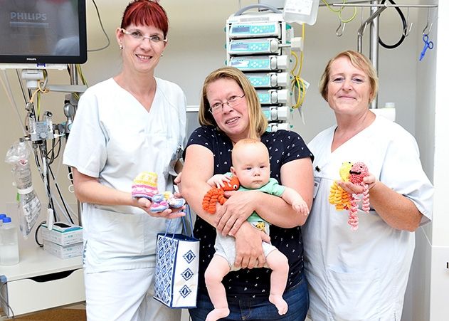 Juliane Weichold mit Sohn Fabian (Mitte) überreicht ihre gehäkelten Werke an Sabine Schwabe, Stationsleitung der E120, und Katja Müller, Teamleitung der E120 am UKJ (v.l.).