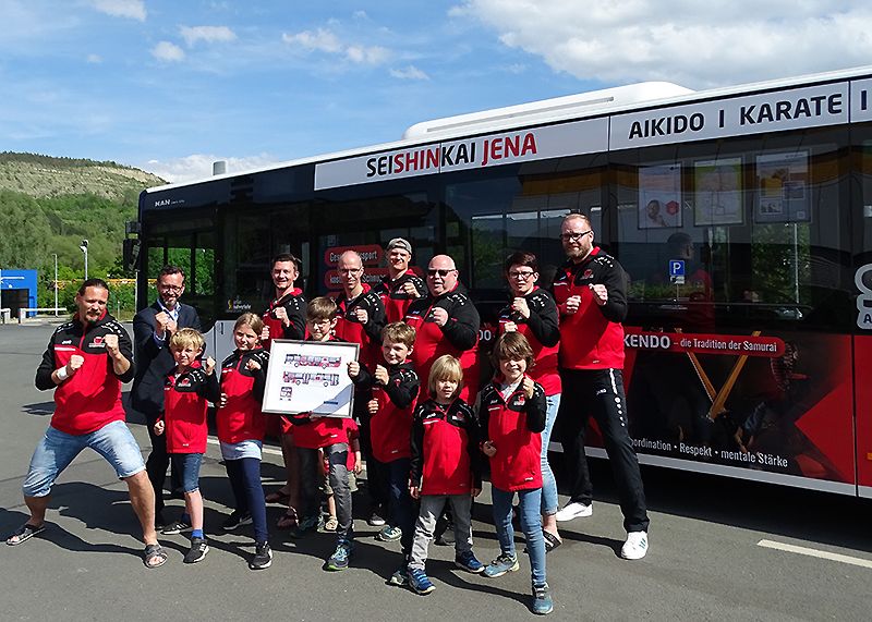 Vereinspräsident Mitja Suck (links im Bild) mit Vereinsmitgliedern sowie Steffen Gundermann, Geschäftsführer des Jenaer Nahverkehrs, (2. v.l.) beim Fotoshooting vor dem neu gestalteten Bus, der ab sofort für den Kampfsportverein durch Jena rollt.