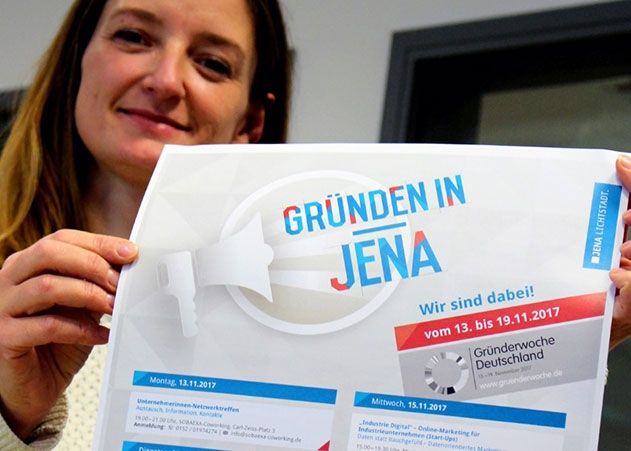 JenaWirtschaft-Mitarbeiterin Nina Machens präsentiert das Plakat zur Gründerwoche in Jena.