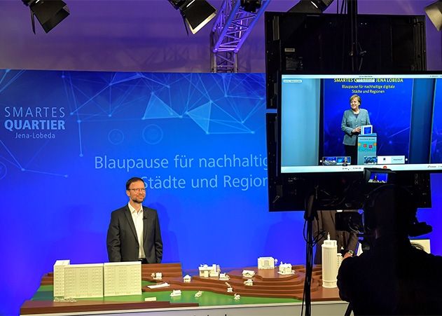 Jenas Oberbürgermeister Dr. Thomas Nitzsche erläutert Bundeskanzlerin Angela Merkel im digitalen Studio, wie das Smarte Quartier Jena-Lobeda als Blaupause für nachhaltige digitale Städte und Regionen dienen kann.